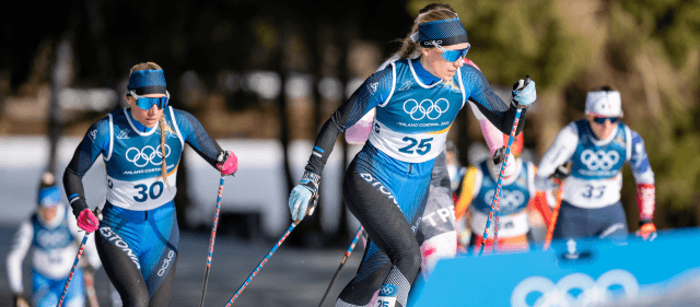 Estonian cross-country skiers in blue Olympic suits compete on a snowy track with ski poles.