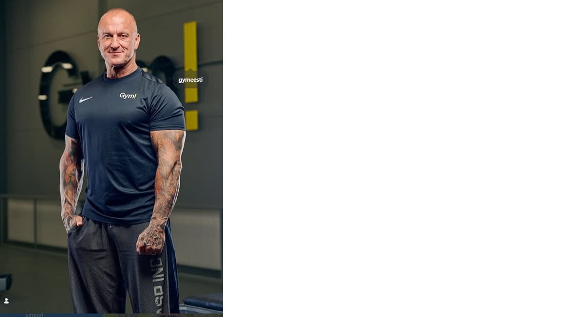 Muscular bald man with tattooed arms posing in a gym wearing a navy shirt.