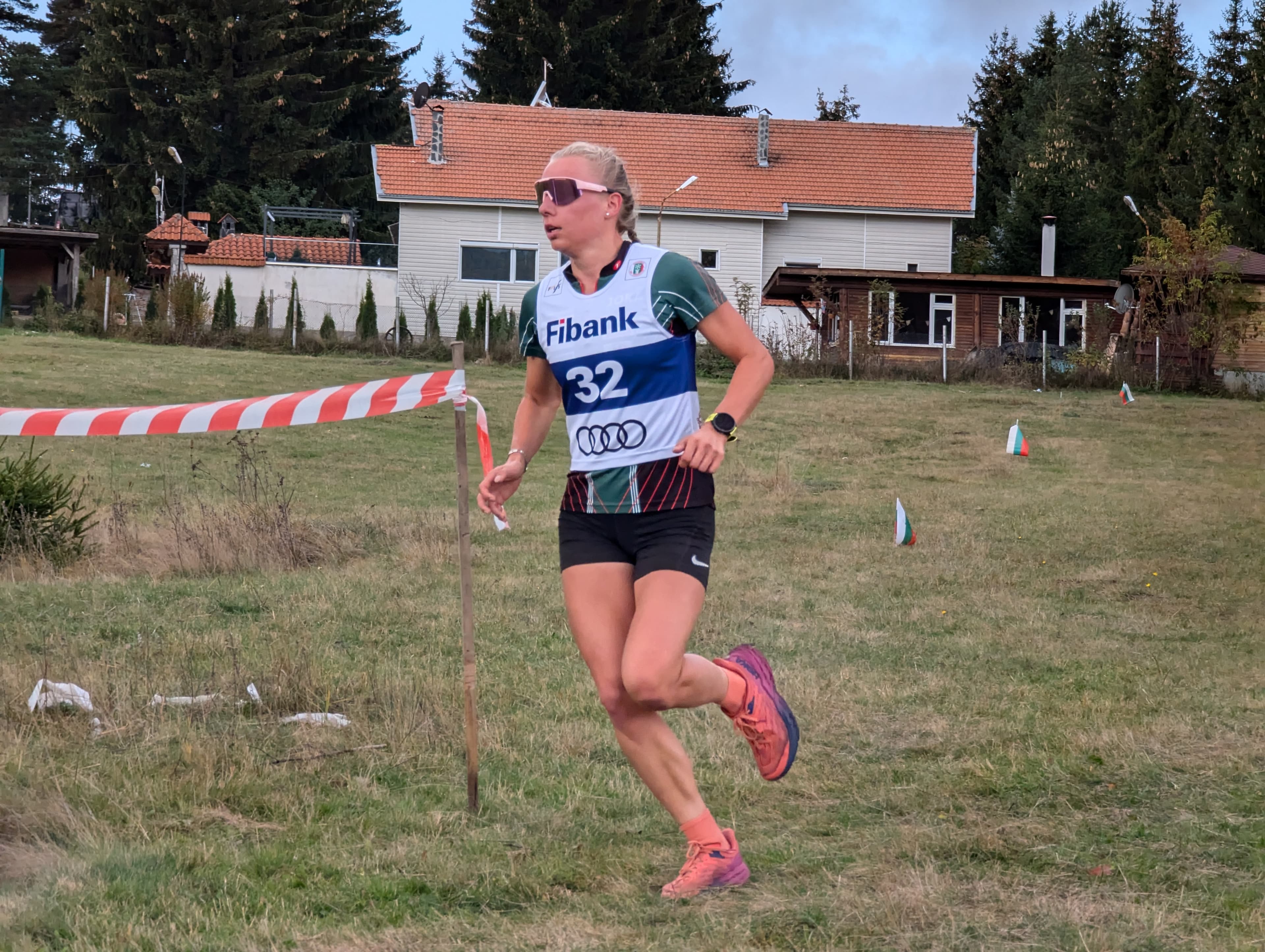 Female runner wearing bib 32 sprints across a grassy field during an outdoor race.