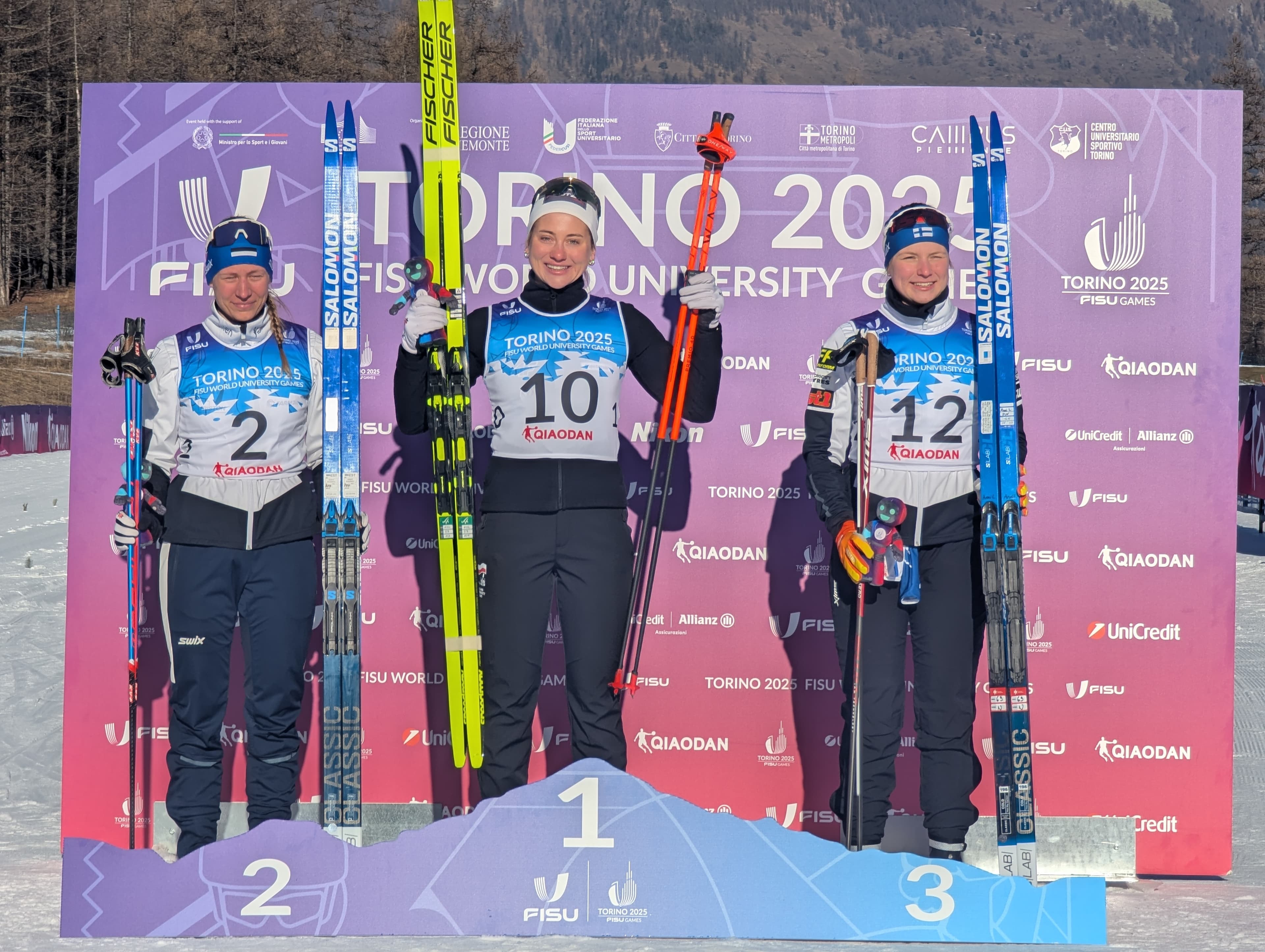 Three female cross-country skiers pose on a podium at the Torino 2025 FISU Games.