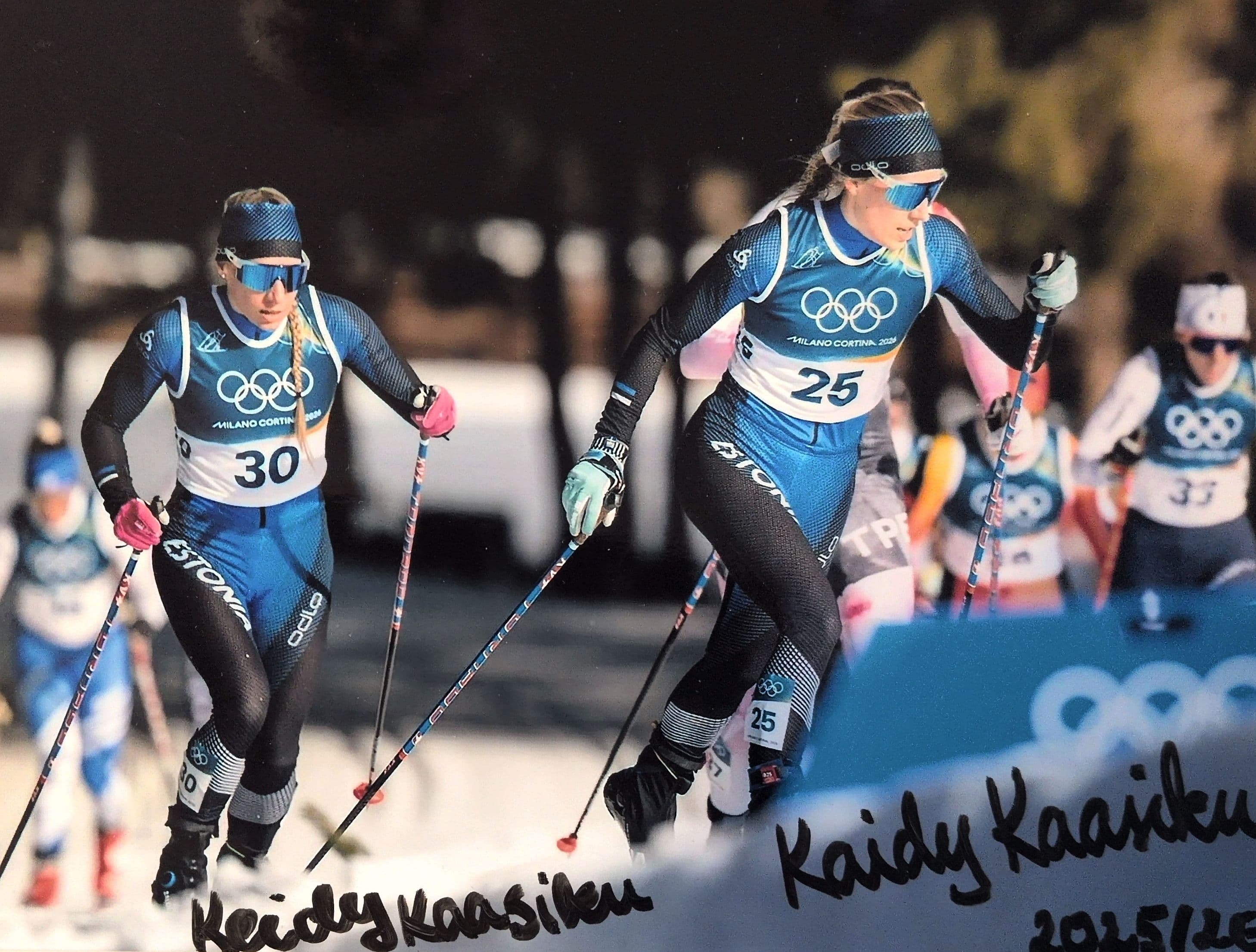 Two female cross-country skiers in blue uniforms race during the Milano Cortina 2026 Olympics.