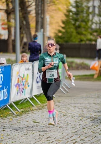 Female orienteer wearing bib 49 runs on a cobblestone path while holding a race map.